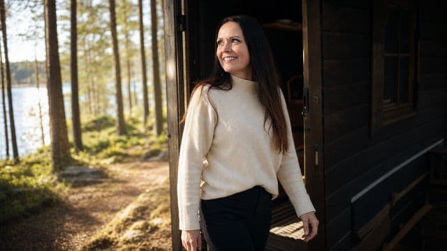 Maisa astuu hämärästä mökistä kirkkaaseen aamuaurinkoon.